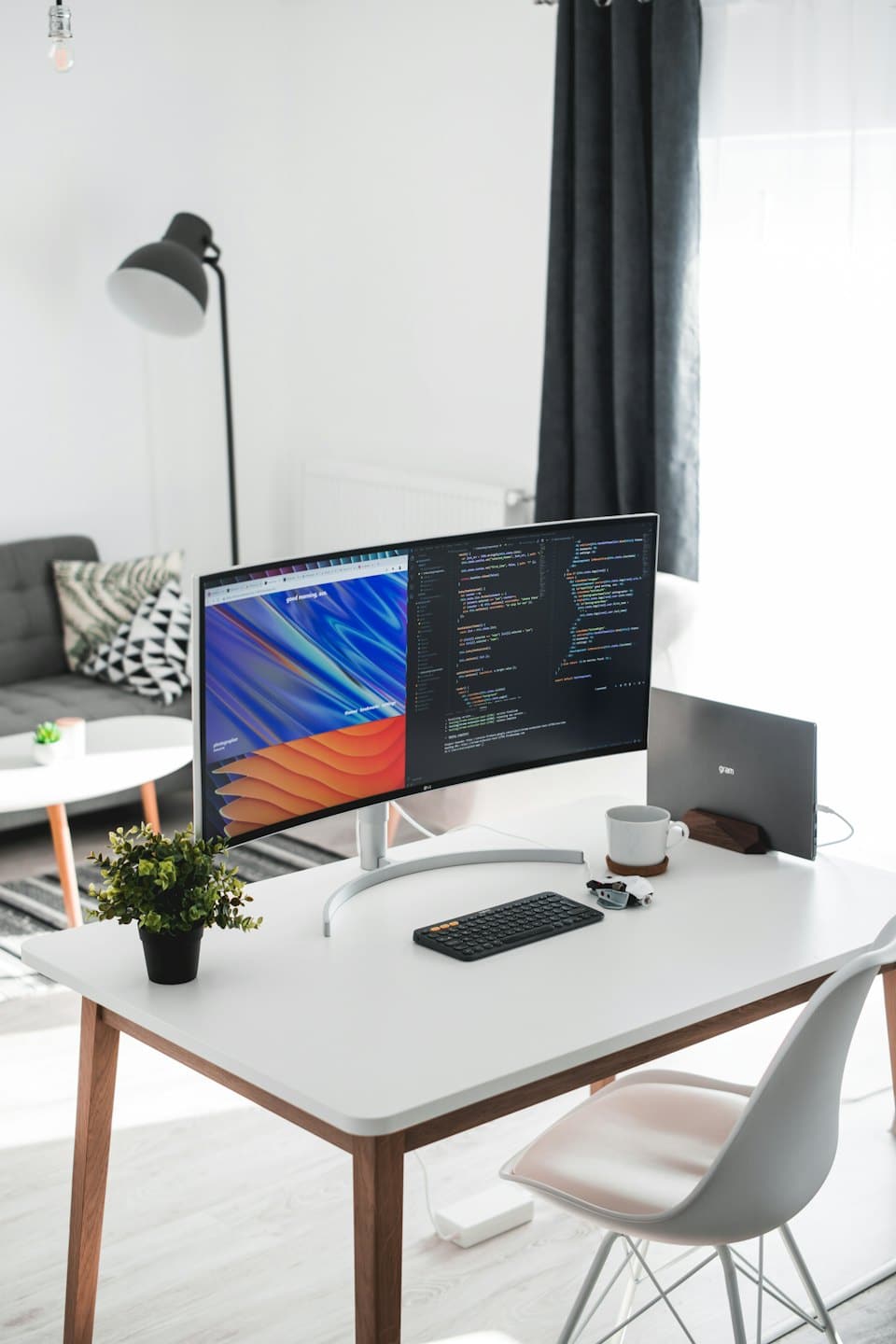 Monitor ultrawide i laptop na nowoczesnym biurku z rośliną.